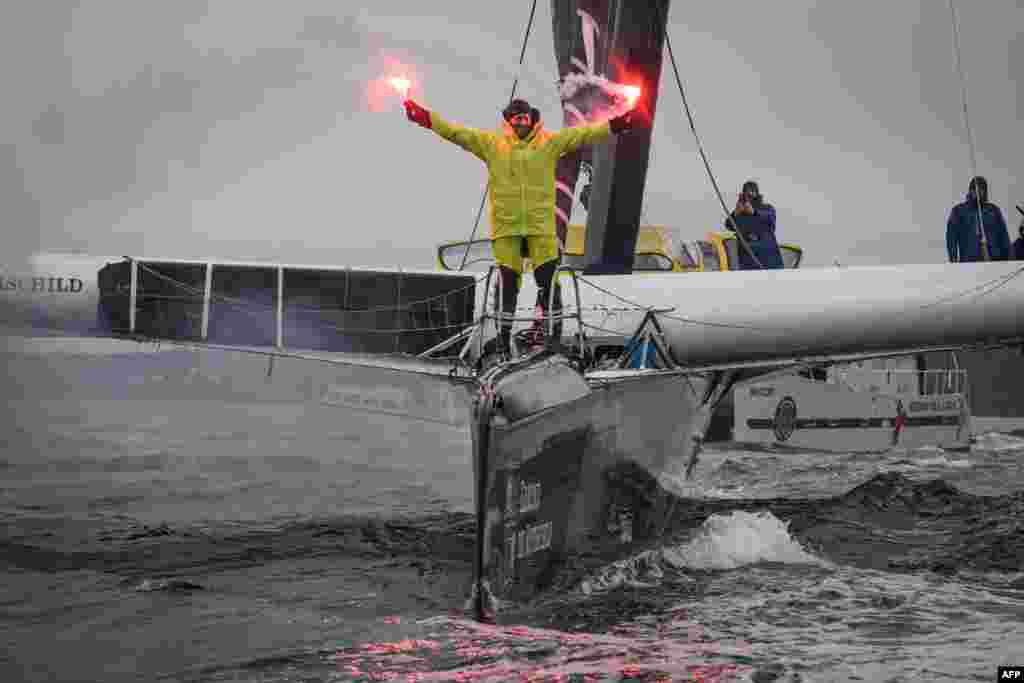 French skipper Charles Caudrelier holds burning flares onboard his Ultim multihull Gitana-Edmond de Rothschild as he sails into a port after winning the Arkea Ultim challenge around-the-world solo sailing race, in Brest, western France.