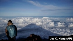 FILE - The shadow of Mount Fuji is cast on clouds hanging below the summit, Tuesday, Aug. 27, 2019, in Japan. Those who want to climb the mountain will now have to reserve ahead and pay a fee. (AP Photo/Jae C. Hong, File)