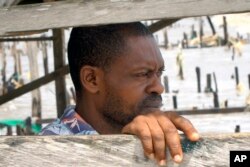 Stephen Tunlese, who lost his house and shop due to coastal erosion, stands inside damaged stilt house looking at the sea in Ayetoro, Southwest Nigeria, Friday, April 5, 2024. (AP Photo/Dan Ikpoyi)