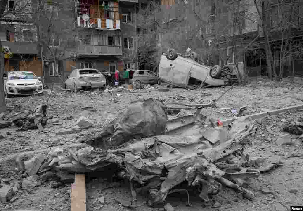 Local residents stand near their apartment building and cars damaged during a Russian missile strike, amid Russia's attack on Ukraine, in Kharkiv, Ukraine.