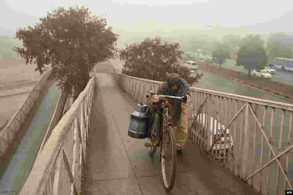 A milkman pushes his bicycle through a pedestrian bridge on a cold foggy winter morning in Islamabad,