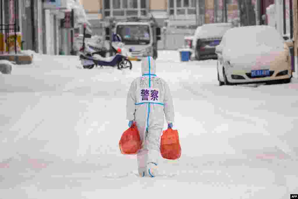 A police officer wearing personal protective equipment carries food and daily supplies that will be distributed to those living in a restricted residential area because of the spread of COVID-19 in Manzhouli in China's northern Inner Mongolia region.