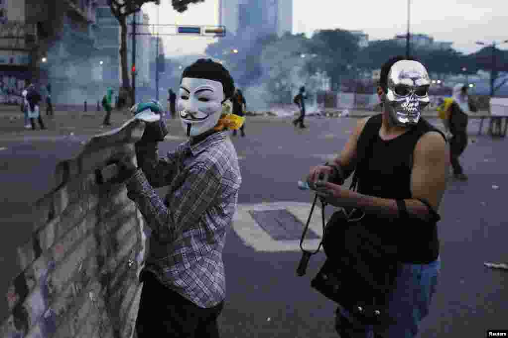 Manifestantes anti-governo mascarados transportam um escudo improvisado durante os confrontos com a polícia na Praça Altamira, em Caracas, Fev. 27, 2014.