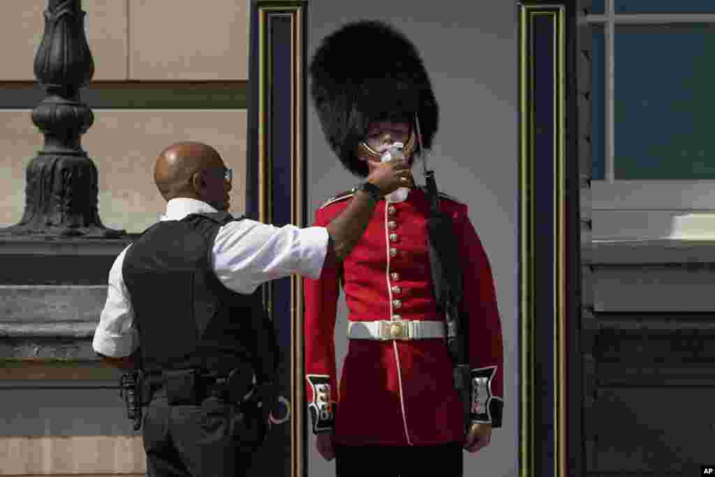 A police officer gives water to a British soldier on guard duty outside Buckingham Palace, during hot weather in London.