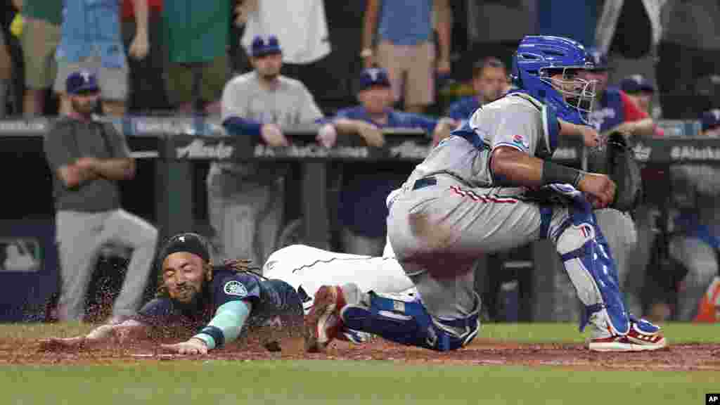 Seattle Mariners' J.P. Crawford slides safely home past Texas Rangers catcher Meibrys Viloria to score the game-tying run on an RBI-double hit by Cal Raleigh during the ninth inning of a baseball game, July 26, 2022, in Seattle, Washington.