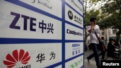 一名中国男子从武汉街头有着华为和中兴标徽的广告牌前走过。