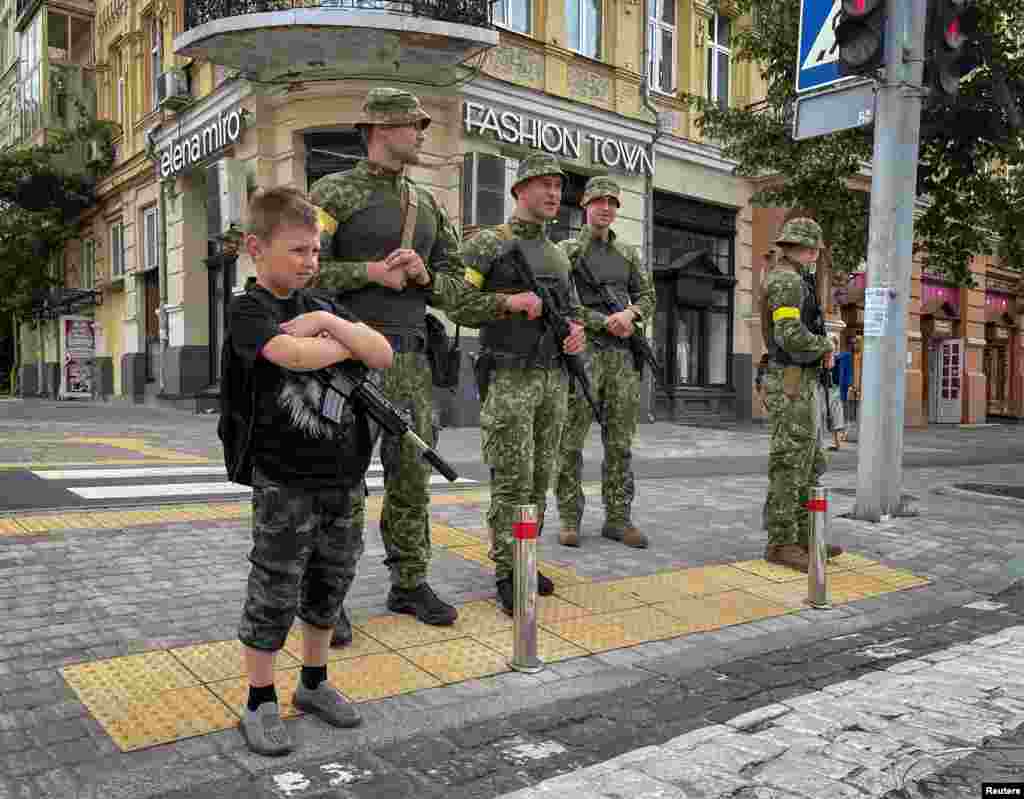 A boy with a toy machine gun stands near Ukrainian servicemen as they patrol an area in central Kyiv, amid Russia's attack on Ukraine, June 22, 2022.