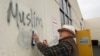 FILE - Tom Garing cleans up racist graffiti painted on the side of a mosque in what officials are calling an apparent hate crime, Feb. 1, 2017, in Roseville, Calif. The Tarbiya Institute was spray-painted with a dozen obscene and racist slurs. 