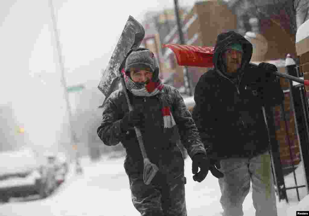 Dois homens carregam pás enquanto caminham sobre uma altura de neve bastante considerável em Detroit, Michigan, Jan. 2, 2014.