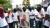 Miembros de una pandilla encabezada por Jimmy Cherizier, alias Berbecue, un expolicía que lidera una coalición de pandillas llamada "Familia G9 y Aliados", transportan un retrato del asesinado presidente Jovenel Moise durante una marcha efectuada el lunes 26 de julio de 2021.