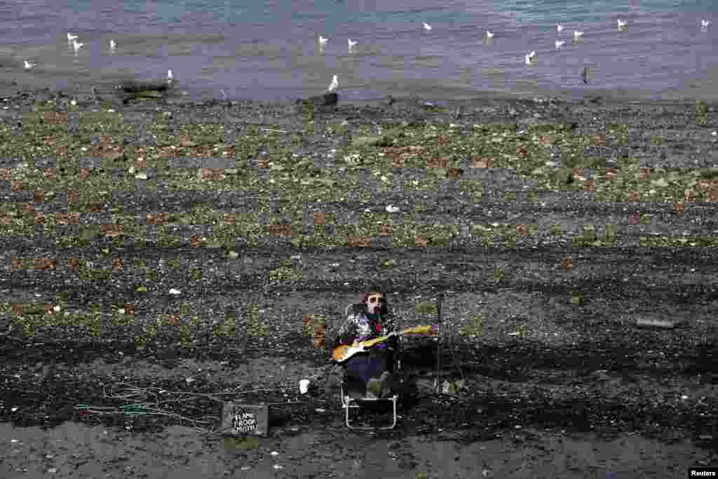 Seorang pengamen memainkan gitar listriknya sambil duduk di tepi selatan Sungai Thames di pusat kota London.