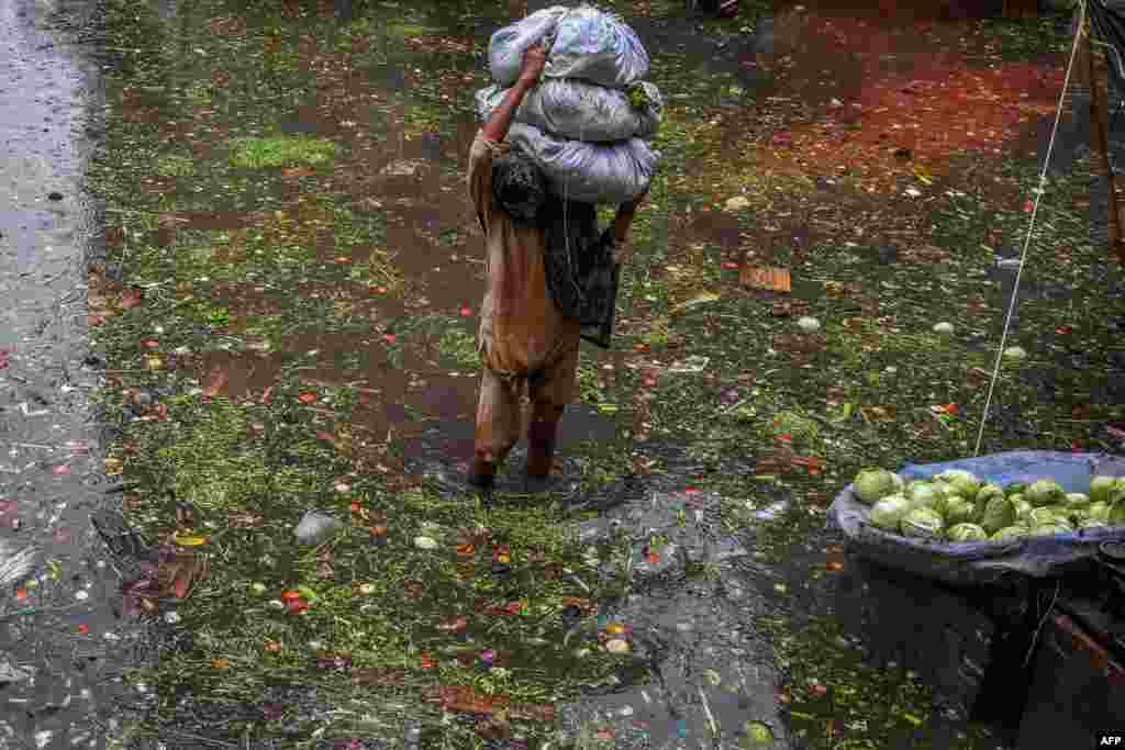 A worker carries vegetables as he wades through a waterlogged street in a market area in Lahore, Pakistan.