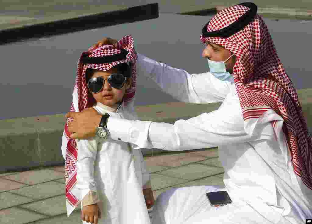A Saudi man arranges his son's traditional "Ghutra," or head cover, after performing Eid al-Fitr prayers marking the end of the holy fasting month of Ramadan in Jiddah, Saudi Arabia.