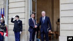 New French prime minister Michel Barnier, right, shakes hands with outgoing prime minister Gabriel Attal during the handover ceremony, Sept. 5, 2024 in Paris. 