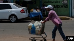 Una mujer empuja un carrito cargado con botellas de agua recolectadas de un grifo improvisado en una calle de Maracaibo, Venezuela, el 25 de mayo de 2020, durante la pandemia del coronavirus COVID-19.