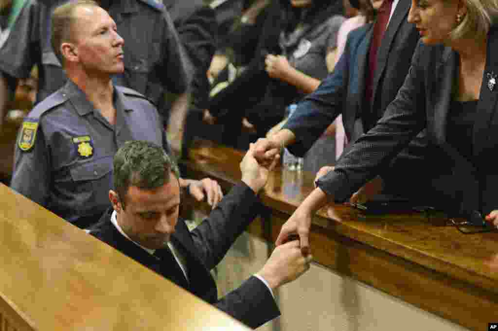 Oscar Pistorius, center, touches hands with family members as he is led down to the cells of the court in Pretoria, South Africa, Oct. 21, 2014.