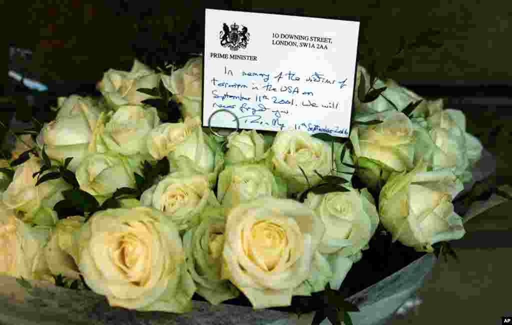 Kartu bertuliskan tangan Perdana Menteri Inggris Theresa May di atas karangan bunga mawar untuk menghormati para warga Inggris yang menjadi korban serangan 9/11 di taman Grosvenor Square dekat Kedutaan Besar AS di London (11/9). (AP/Alastair Grant)
