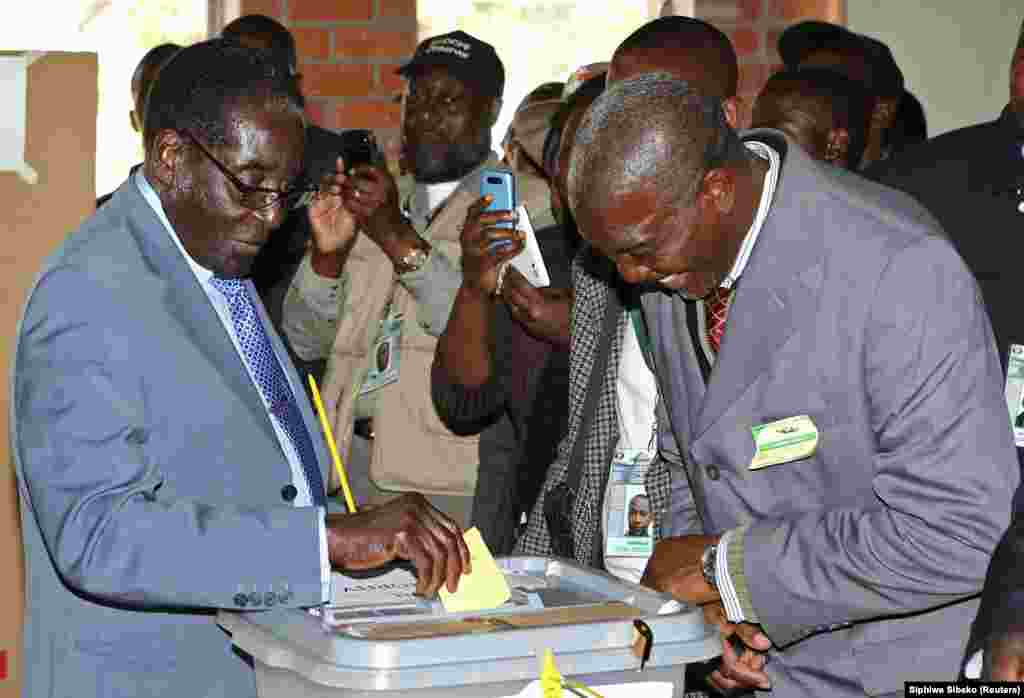 Zimbabwe's President Robert Mugabe (L) cast his vote as an election officer looks on in Highfields outside Harare July 31, 2013.