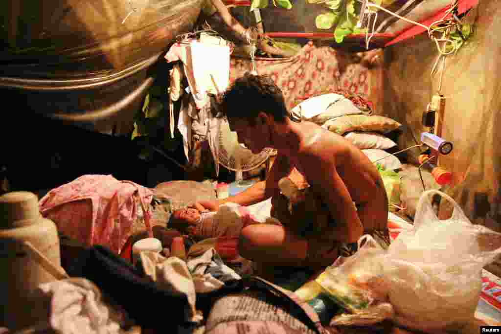 A man feeds his two-month old twins in a tent erected atop a tombstone at the North Cemetery where many victims of the country's war on drugs are buried, in Manila, Philippines.