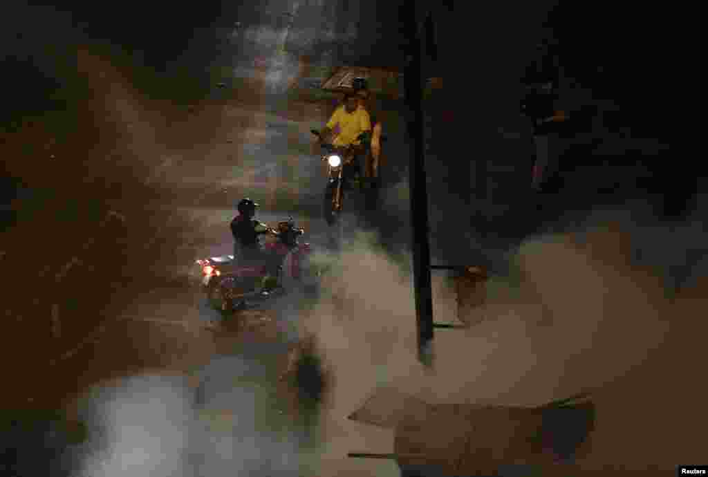 Motociclistas observam os bombeiros a tentar apagar as chamas da motorizadas incendiadas pelos manifestantes anti-governo na Praça de Altamira em Caracas, Fev. 26, 2014. 