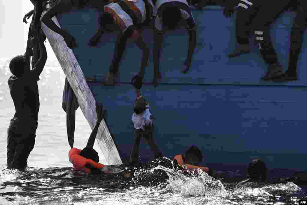 Para migran di atas perahu berusaha menyelamatkan seorang anak kecil yang terkatung-katung di lepas pantai Libya, Laut Tengah.