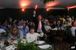 A spotter waves a light stick to signal receipt of a new bid at the Elo de Raça auction in Uberaba, Minas Gerais state, Brazil, Sunday, April 28, 2024. The Elo de Raça is the most prestigious auction at the world’s biggest Zebu fair. (AP Photo/Silvia Izquierdo)
