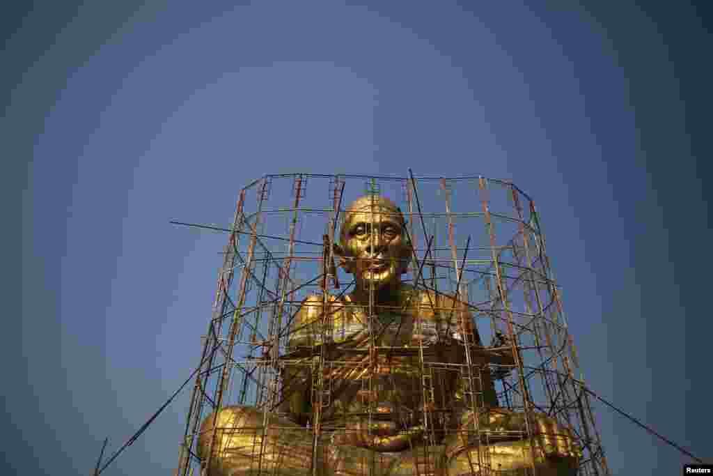Para pekerja memanjat perancah sambil memberikan sentuhan akhir pada patung Buddha raksasa di kuil dekat pasar terapung Amphawa di Provinsi Samut Songkhram, Thailand.