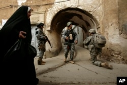 FILE - An Iraqi woman passes U.S. troops and Iraqi police officers as they stand guard in the Bab al-Jadeed area of Mosul, 360 kilometers (225 miles) northwest of Baghdad, Iraq.