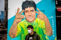 El pintor Daniel Manrique se para frente a su mural que representa a Lutz Sherlock, una presunta víctima de COVID-19.