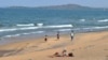 A woman reads a book as young boys pass by on the Saga beach at Lake Malawi, July 17, 2011. 
