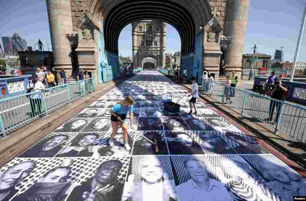 Workers place portraits of Londoners, including London's Mayor Sadiq Khan, by French artist JR, on the road at Tower Bridge to celebrate UEFA Euro 2020, in London.