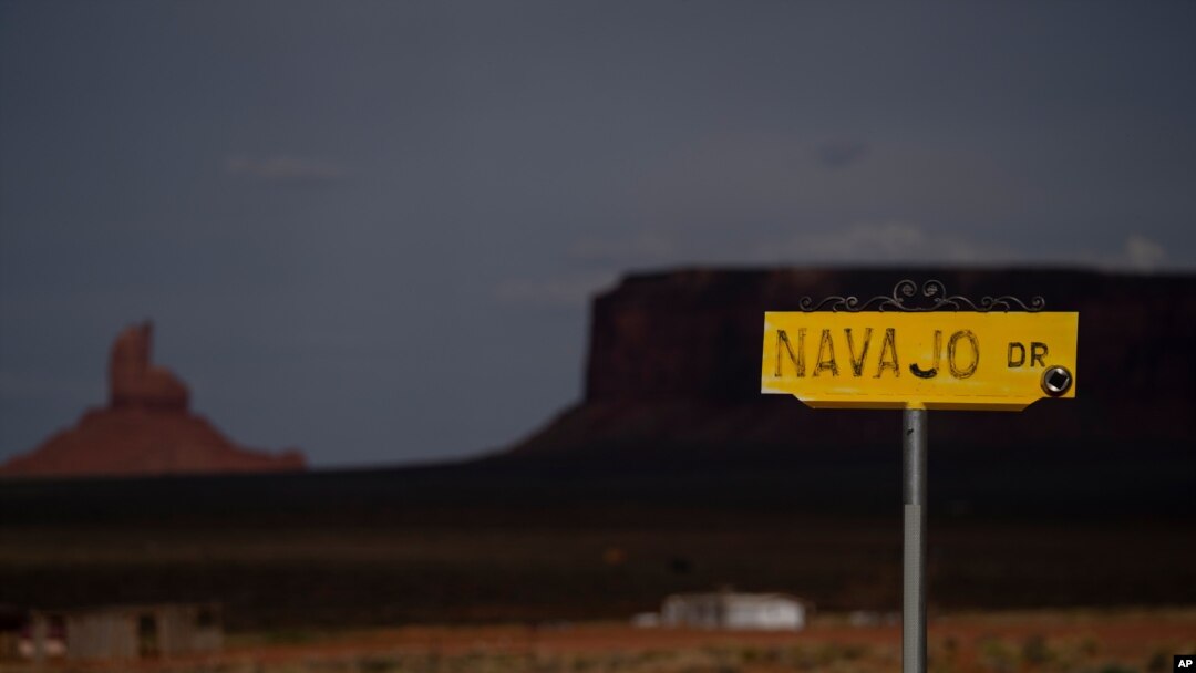 FILE - A sign for Navajo Drive is seen against cloud-darkened Oljato-Monument Valley, Utah, on the Navajo Reservation, April 30, 2020. Across the nation, Native American tribes are working to protect their oldest members from COVID. 