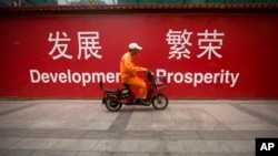 在北京市中心的一条街道上，一名维修工人骑着摩托车经过用中英文书写的“发展”和“繁荣”的标语（2015年7月15日）。