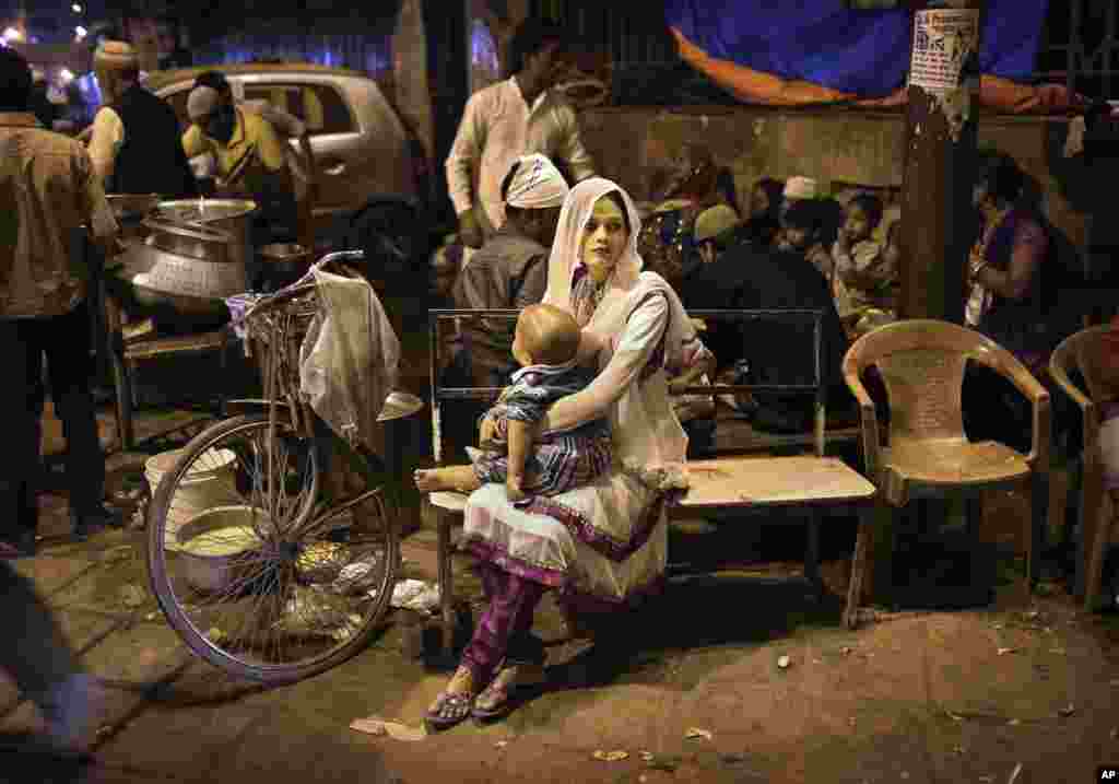 Seorang wanita Muslim India menggendong bayinya saat menunggu di bangku sebuah warung makanan di New Delhi.