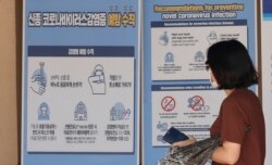 Una visitante con una mascarilla camina cerca de una pancarta que muestra las precauciones contra el coronavirus en el Palacio Gyeongbok, uno de los monumentos más conocidos de Corea del Sur, en Seúl, Corea del Sur, el domingo 16 de agosto de 2020.